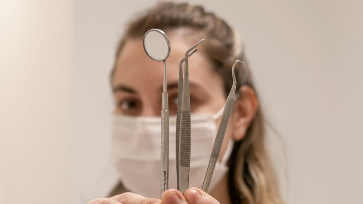 Odontóloga sosteniendo el espejo, la pinza y el explorador que se usan en una limpieza dental.